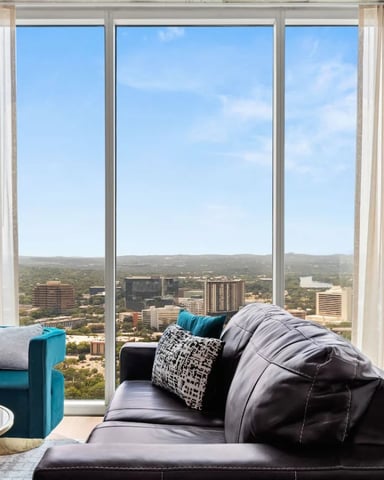 High-rise living room with floor-to-ceiling windows overlooking cityscape, downtown buildings, and green landscape below