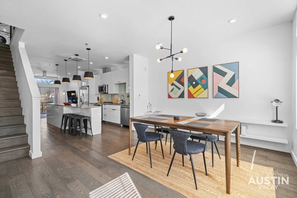 Open-plan kitchen and dining area with wood table, gray chairs, white cabinetry, and geometric wall art