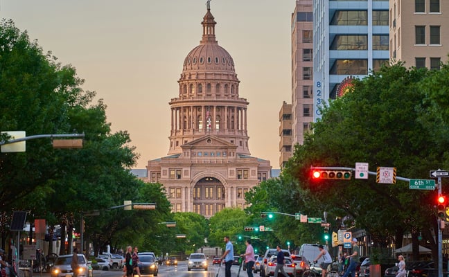 Congress Avenue at golden hour with pedestrians crossing and the Texas State Capitol dome glowing in the background