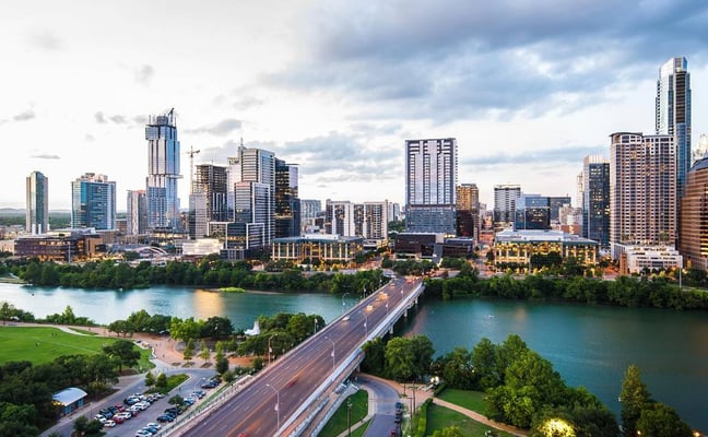 Downtown skyline with high-rise buildings overlooking turquoise river, bridge, and green parkland below